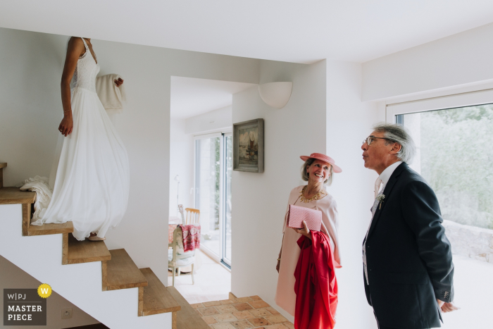Photo by: <a href="https://www.wpja.com/contests/2018-v06-photography-competition/best-wedding-photographers/2211686">Christophe Pasteur - Lorient </a> The bride's mother and father wait downstairs as she makes her way from above
