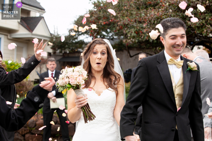 Photo by: <a href="https://www.wpja.com/contests/2018-v06-photography-competition/best-wedding-photographers/2213246">Joyce Perlman - San Francisco California</a> The bride reacts to flower petals in the air as she walks out of the ceremony with her new husband at the MacCallum House Inn, Mendocino, CA