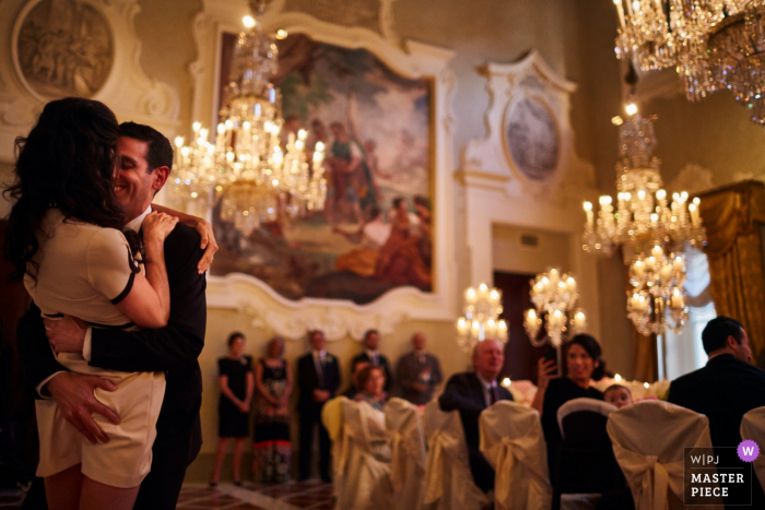 Elegantes Hochzeitsempfangsbild in der Toskana, auf dem Braut und Bräutigam ihren ersten Tanz mit unter Kronleuchtern sitzenden Gästen feiern