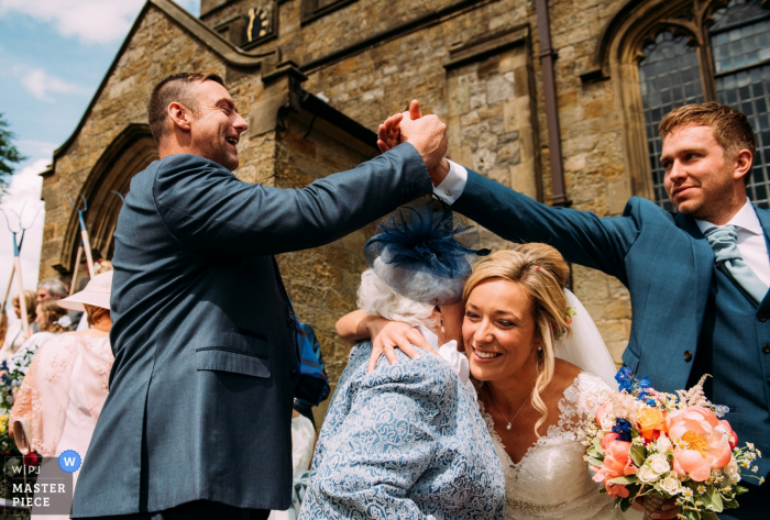 Photo by: <a href="https://www.wpja.com/contests/2018-v06-photography-competition/best-wedding-photographers/2214506">David Scholes - Clitheroe Lancashire</a> Outdoor photo of groom and guest shaking hands while bride hugs woman after the wedding in Ribble valley, Uk