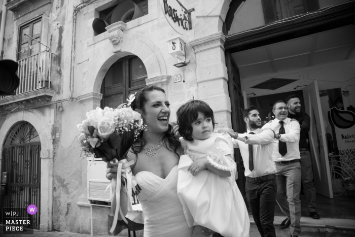 La novia sostiene a la niña de las flores afuera después de la ceremonia de boda en Siracusa