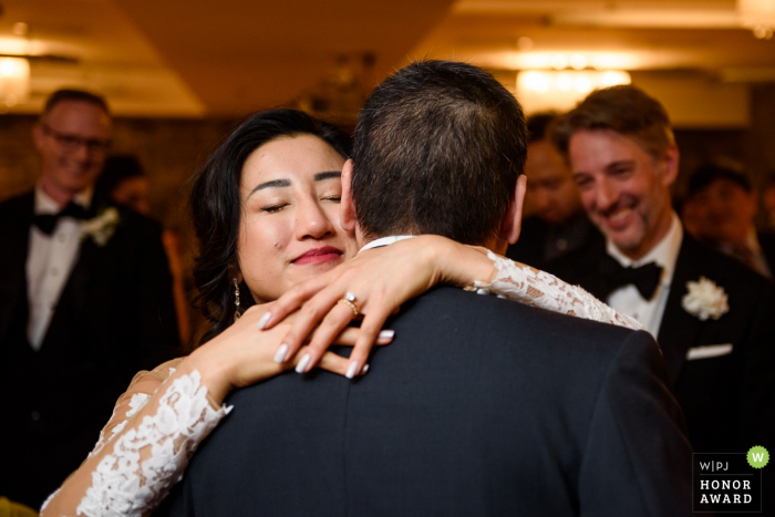 Foto: <a href="https://www.wpja.com/contests/2018-v08-Fotowettbewerb/Best-wedding-Photographier/2237066"> Esther Gibbons - Montreal Quebec </a> Montréal Québec Braut umarmt ihren Vater, während der Bräutigam lächelt