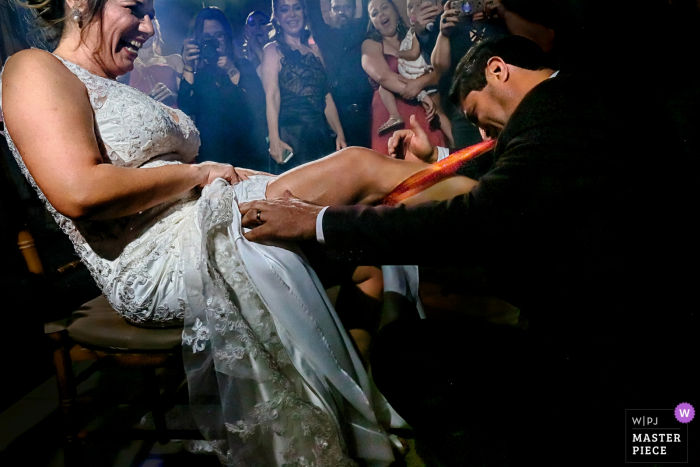 Groom getting the garter from the bride's leg Groom getting the garter from the bride at the wedding reception in Goiânia