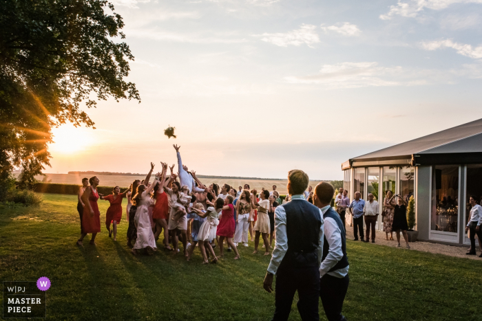 Photo by: <a href="https://www.wpja.com/contests/2018-v09/best-wedding-photographers/2238756">Henri Deroche - Orléans </a> Outdoor photo of guests reaching for the bouquet at the sunset wedding reception in Dangy Centre Val De Loire