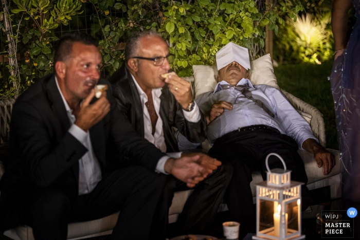 Guest sleeps on the couch next to people eating at the wedding reception in Calabria