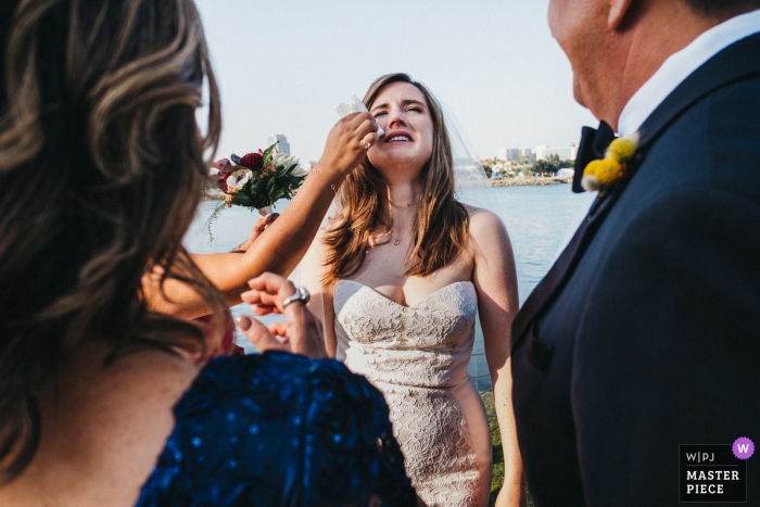 Bride getting something wiped off her face outside at the wedding in Long Beach, California, USA