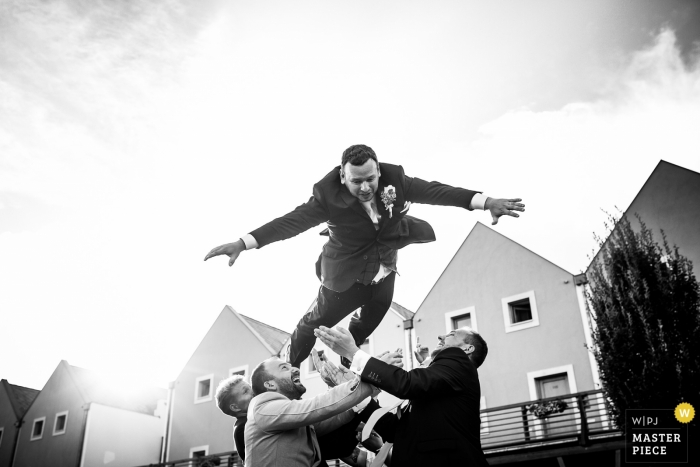 Groomsmen throw the groom into the air outside at the wedding reception in Prague