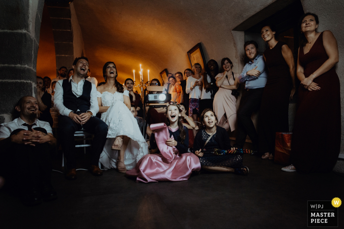 The bride, groom, and guests sit around a room laughing in the Chateau de Saulnat in this photo by a Lyon wedding photographer.