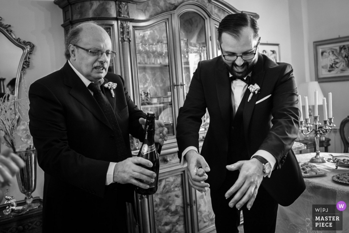 Zdjęcie: <a href="https://www.wpja.com/contests/2018-v10-photography-competition/best-wedding-photographers/2249356"> Claudio Valerio - Cosenza Reggio Calabria </a> Czarno-białe zdjęcie dwóch mężczyzn otwierających butelkę szampana w jadalni przez fotografa ślubnego Cosenza.