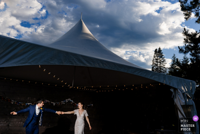 The bride and groom hold hands in front of a large tent in Leavenworth, WA in this photo by a Seattle wedding photographer.