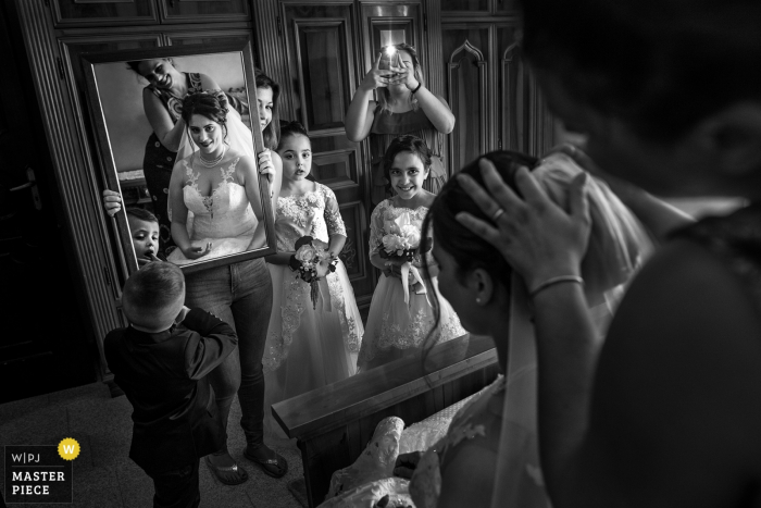 Photo by: <a href="https://www.wpja.com/contests/2018-v10/best-wedding-photographers/2252976">Pasquale Minniti - Reggio Calabria</a> A mirror is held up for the bride as members of the bridal party watch her and take photos in this black and white photo by a Calabria wedding photographer.