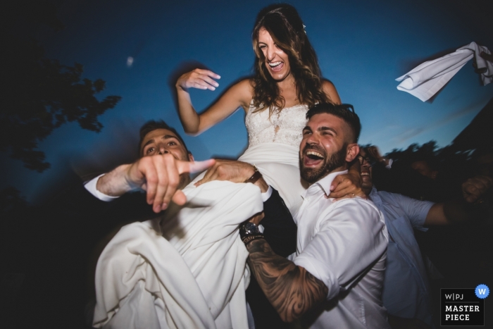 Lucca wedding picture of the bride riding on the shoulders of guys outside.