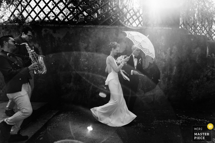 Lisbon Wedding Photojournalist | the bride with a white umbrella under the sun in a black and white image with the saxophone