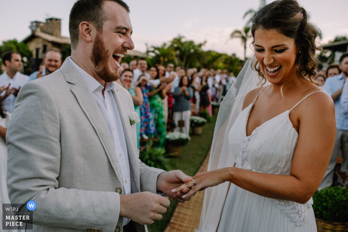 Praia do Rosa - Santa Catarina - Brasilien L Hochzeit Foto des Bräutigams, der im Begriff ist, den Ring auf den Brautfinger in diesem Hochzeitszeremoniebild im Freien zu setzen