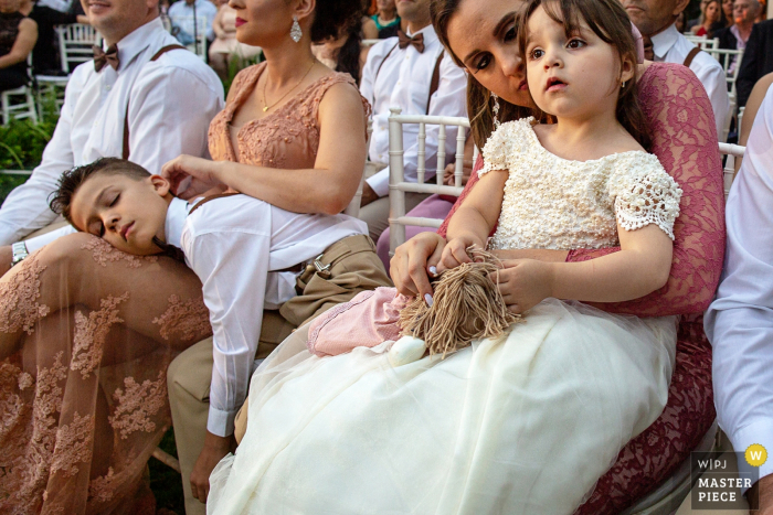 a flower girl and ring bearer patiently wait through a long outdoor wedding ceremony Goiânia flower girl and ring bearer patiently wait through a long outdoor wedding ceremony on the grass
