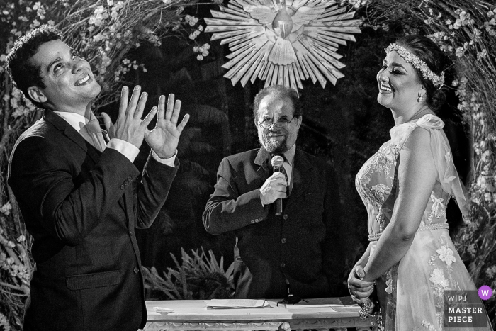 Goiânia Wedding Photojournalist | the bride and groom with the officiant in a black-and-white ceremony image