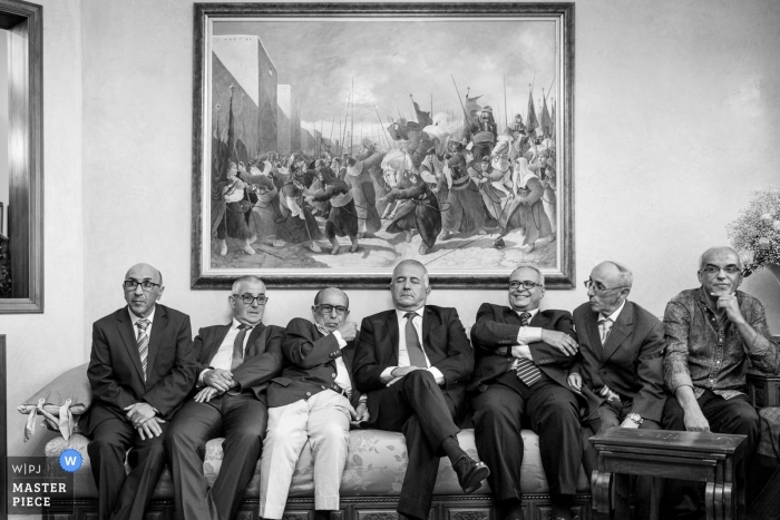Photo by: <a href="https://www.wpja.com/contests/2018-v12/best-wedding-photographers/2274226">Simon Cassanas - Paris </a> Paris Wedding Photojournalist | a group of elderly men are seated on the big couch under a painting at the reception