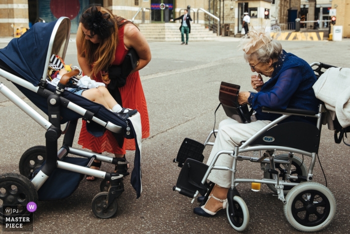  HAC, London  Wedding Photojournalist | grandma in wheelchair is facing a baby in a stroller outside of the church wedding