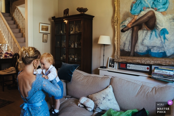 Photo by: <a href="https://www.wpja.com/contests/2018-v12/best-wedding-photographers/2278716">Lyndsey Goddard - London London</a> London Wedding Photojournalist | a very young toddler is getting dressed for the wedding ceremony with the help of a bridesmaid in a blue dress