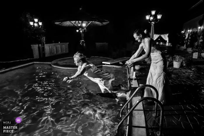 Photo by: <a href="https://www.wpja.com/contests/2018-v12/best-wedding-photographers/2279211">Elena Haralabaki - Nea Ionia Attica</a> Athens Wedding Photojournalist | the bride pushes a woman into the pool at this outdoor night wedding reception party