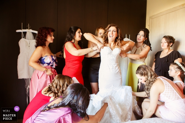 Foto door: <a href="https://www.wpja.com/contests/2018-v13/best-wedding-fotografen/2281376"> Vasilis Maneas - Thessaloniki </a> Veria Wedding Fotojournalist | de bruid heeft meerdere handen en helpt haar in haar jurk te passen