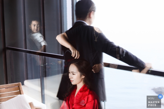 Photo by: <a href="https://www.wpja.com/contests/2018-v13/best-wedding-photographers/2281621">Mango Gu - Hangzhou </a> Hangzhou City Wedding Photojournalist | the bride has her hair prepared for the ceremony as her groom waits as visible in the reflection