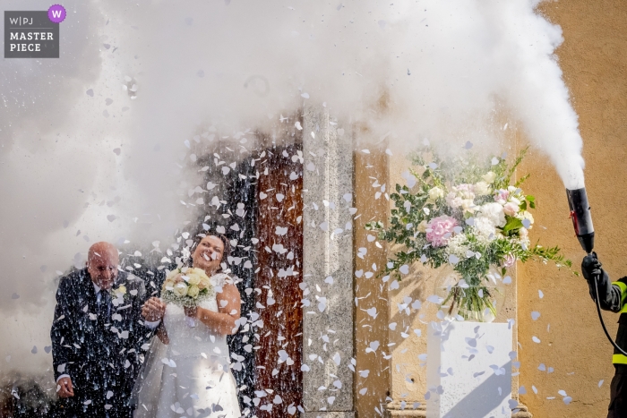 Foto door: <a href="https://www.wpja.com/contests/2018-v13/best-wedding-fotografen/2281861"> Luigi Rota - Comomeer Lecco </a> Lecco Wedding Fotojournalist | de bruid en bruidegom verlaten de kerk en worden bespoten door een brandweerman met behulp van een brandblusser