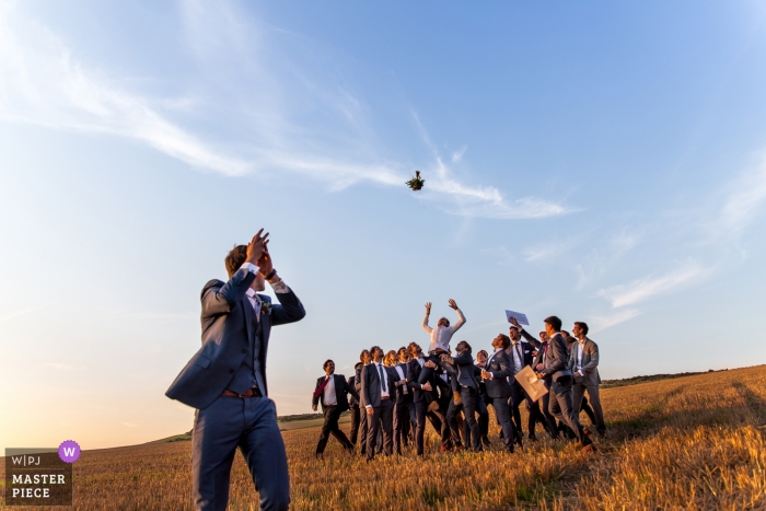 Photo by: <a href="https://www.wpja.com/contests/2018-v13/best-wedding-photographers/2282586">David Merat - Lille </a> Wissant Wedding Photojournalist | the groom tosses the brides bouquet to a group of men outside on a hill