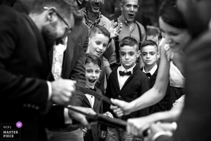 Photo by: <a href="https://www.wpja.com/contests/2018-v13/best-wedding-photographers/2283111">Sergio Bruno - Manta </a> Cherasco Wedding Photojournalist | Black and white photo of boys watching the bride and groom saw a log together