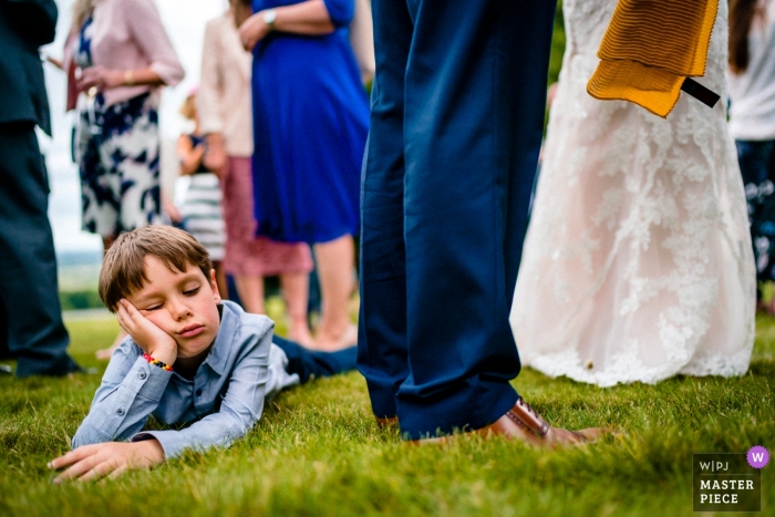 Photo by: <a href="https://www.wpja.com/contests/2018-v13/best-wedding-photographers/2286491">Paul Rogers - Hitchin Hertfordshire</a> Boughton Monchelsea Place, UK wedding photograph of a bored boy lying on the reception grass.