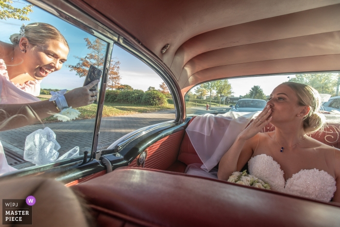 Photo by: <a href="https://www.wpja.com/contests/2018-v15/best-wedding-photographers/2304506">Nicolas Bernard - Ammerschwihr </a> The bride blows kisses to A phone yielding a bridesmaid from the rear Seat of a vintage car in Plobsheim, France