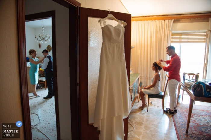 Foto di: <a href="https://www.wpja.com/contests/2018-v15/best-wedding-photographers/2310171"> Alessandro Castelli - Siracusa </a> La sposa di Siracusa si è sistemata i capelli mentre il suo vestito pende da una porta