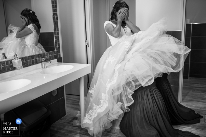 Photo by: <a href="https://www.wpja.com/contests/2018-v15/best-wedding-photographers/2311616">Valerie Teppe - Limoges </a> France Hauterive bride getting help under her dress from bridesmaids in a public restroom