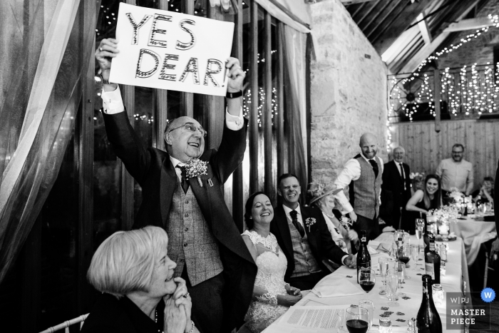 Foto por: <a href="https://www.wpja.com/contests/2018-v16/best-wedding-photographers/2325176"> Aaron Storry - Kettering Northamptonshire </a> Pátio do país de Kingston, Wareham, fotografia BRITÂNICA do casamento do convidado que sustenta "sim o sinal handmade caro" na recepção.