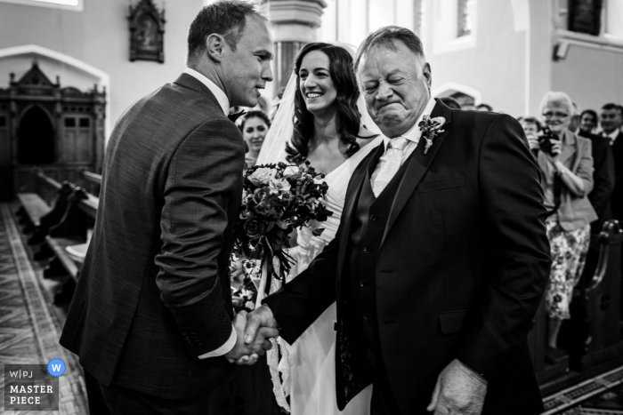 Fotografia do casamento de Meath, Ireland do pai da noiva que agita as mãos com o noivo no altar da cerimônia.