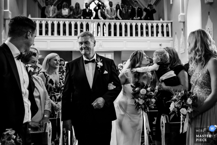 Tipperary, Irlanda Fotografía de boda de novia besando a un bebé mientras camina hacia la iglesia con su padre.