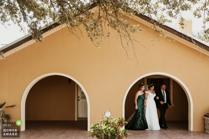 Photo: <a href="https://www.wpja.com/contests/2018-v16-photography-competition/best-wedding-photographers/2329351"> Philip Thomas - San Antonio Texas </a> Photographie documentaire de mariage d'une épouse et de ses parents sortant d'un bâtiment voûté à Mission, au Texas