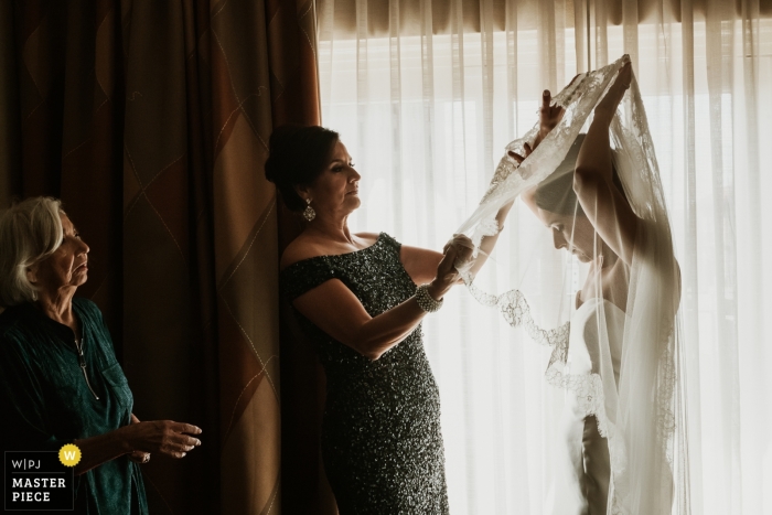 Foto von: <a href="https://www.wpja.com/contests/2018-v16/best-wedding-photographers/2329376"> Philip Thomas - San Antonio Texas </a> San Antonio, Texas dokumentarisches Hochzeitsfoto einer Braut, die Hilfe von den Müttern mit ihrem Schleier empfängt