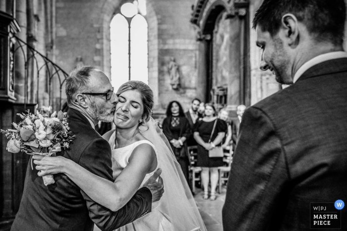 Foto door: <a href="https://www.wpja.com/contests/2018-v17/best-wedding-fotografen/2333056"> Julien Roman - Parijs </a> Les Andelys huwelijksfoto's van een bruid die een kus ontvangt van haar vader in de kerk