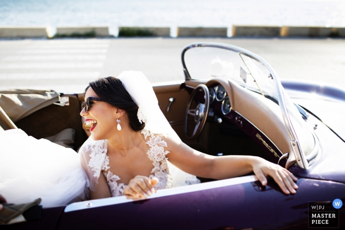 Photo by: <a href="https://www.wpja.com/contests/2018-v17/best-wedding-photographers/2334761">Nino Lombardo - Taormina Trapani</a> Wedding picture of a bride in the passenger seat of a purple convertible auto looking back and laughing - Marsala, Sicilia photographer