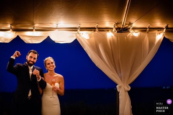 Foto: <a href="https://www.wpja.com/contests/2018-v17/best-wedding-photographers/2343291"> Megan Hannah - Lincoln Vermont </a> Paar Falmouths, Massachusetts während ihrer Hochzeit - pumpt Faust des Bräutigams während der Reden und röstet innerhalb der Zelthochzeit