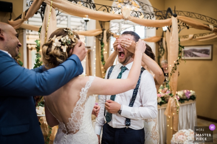 Foto von: <a href="https://www.wpja.com/contests/2018-v18/best-wedding-photographers/2349896"> Hristina Handzhieva - Lovech </a> Lovech Hochzeit schießen mit einem Paar lachend mit ihren Augen von Gästen bedeckt