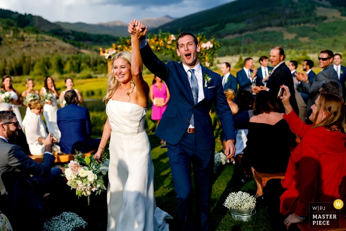 Photo by: <a href="https://www.wpja.com/contests/2018-v18/best-wedding-photographers/2351311">Trent Gillespie - Silverthorne Colorado</a> Bride & groom celebrate while receding down the Camp Hale, CO isle.