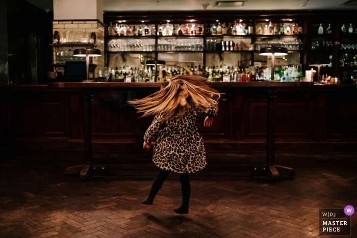 Foto por: <a href="https://www.wpja.com/contests/2018-v18/best-wedding-photographers/2355551"> Kristian Leven - Londres </a> Londres documental foto de boda de niña bailando cerca de bar