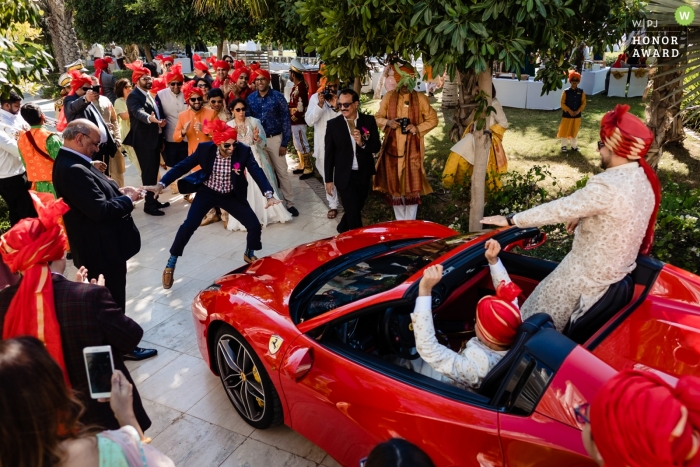 Waldorf Astoria Dubai trouwfoto | huwelijksfoto van de bruidegom die aankomt in een rode cabrio Ferrari als mannen dansen voor de auto