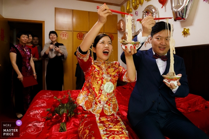 Foto por: <a href="https://www.wpja.com/contests/2018-v18/best-wedding-photographers/2359156"> Vincent Mu - De Zhou </a> Imagen de fotoperiodismo de una boda en Shandong de una pareja disfrutando de fideos junto con palillos en la cama