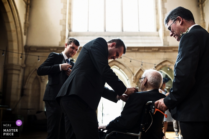 Photo by: <a href="https://www.wpja.com/contests/2018-v18/best-wedding-photographers/2361621">Richard Galloway - Frimley Green Surrey</a> Documentary wedding photograph at Surrey ceremony of man in wheelchair getting help with flowers