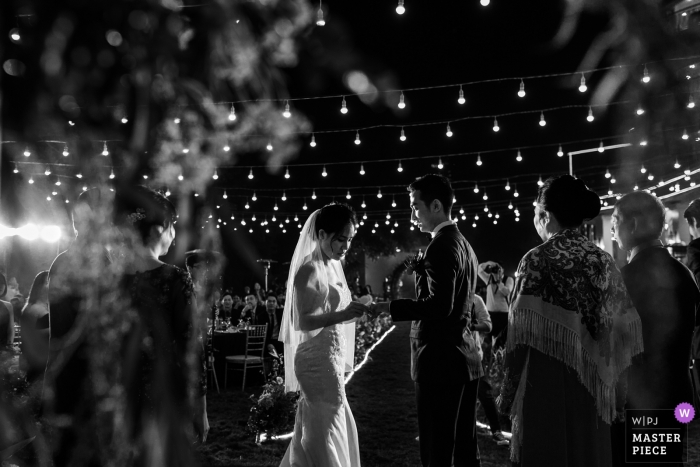 Photo by: <a href="https://www.wpja.com/contests/2018-v19/best-wedding-photographers/2374181">Lucas Tran - Hai Chau Da Nang</a> Ha Noi wedding photojournalism black and white image of a couple exchanging rings during lit ceremony