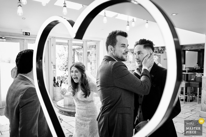 Foto: <a href="https://www.wpja.com/contests/2018-v19/best-wedding-photographers/2375231"> Ian Bursill - Loughborough Leicestershire </a> Mythe Barn, Atherstone, Großbritannien | Braut und Bräutigam, die mit Freunden an der Aufnahme lachen