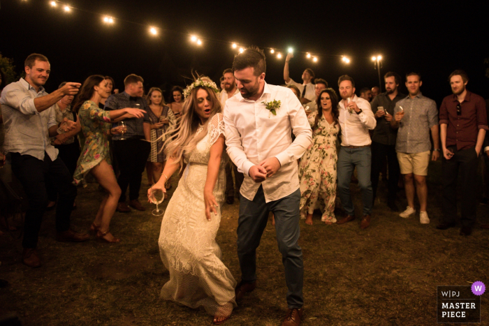 Victoria - AU wedding photojournalism image of a couple dancing during outdoor reception under strings of lights